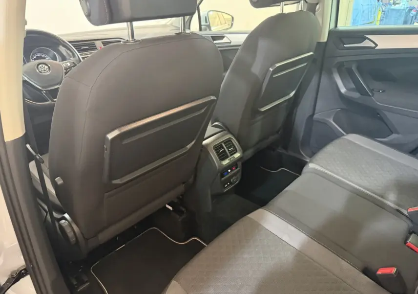 Vue intérieure arrière du Volkswagen Tiguan 2020 montrant les sièges noirs, les dossiers avec tablettes rabattables et la console centrale avec aérateurs.