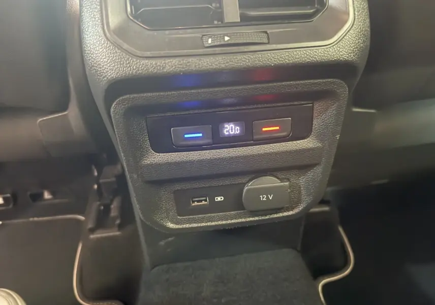 Gros plan sur la console arrière du Volkswagen Tiguan gris clair, avec commandes climatisation et prises USB et 12V visibles.