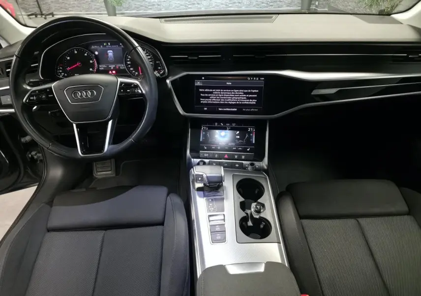 Vue intérieure avant de l'Audi A6 2022 S line, tableau de bord noir avec écran tactile et volant multifonction cuir.