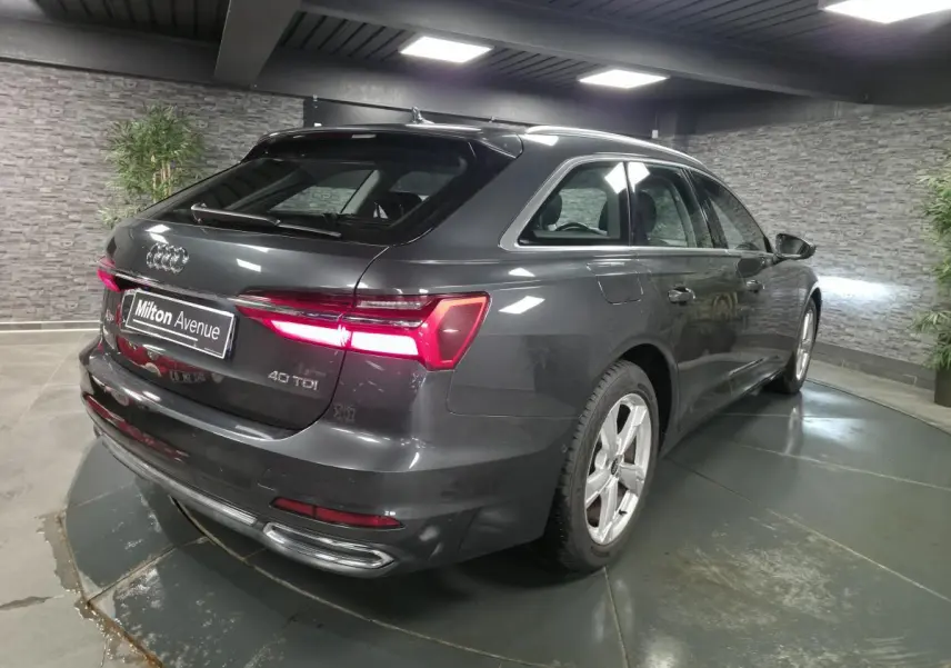 Audi A6 Avant gris en 3/4 arrière droit, feux LED allumés et jantes 5 branches dans un showroom intérieur.