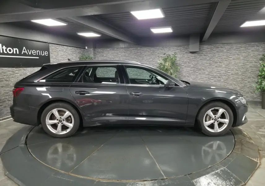Audi A6 Avant gris en profil droit dans un showroom avec jantes 5 branches et toit ouvrant visible.