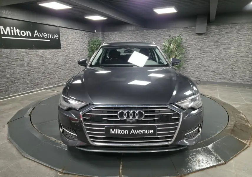 Audi A6 Avant gris vue de face dans un showroom avec calandre chromée et logo Audi visible.