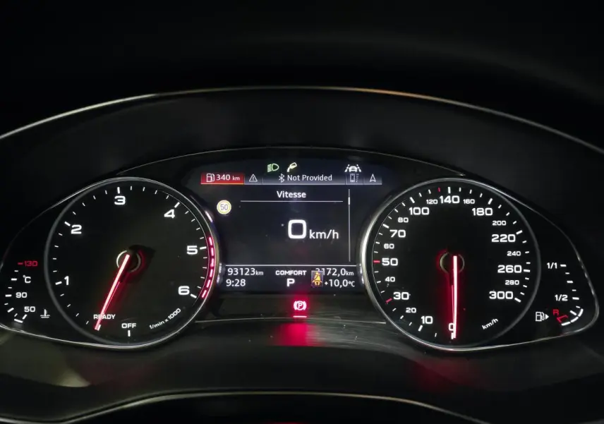 Vue rapprochée du tableau de bord numérique de l'Audi A6 gris, affichant la vitesse à 0 km/h et divers indicateurs.