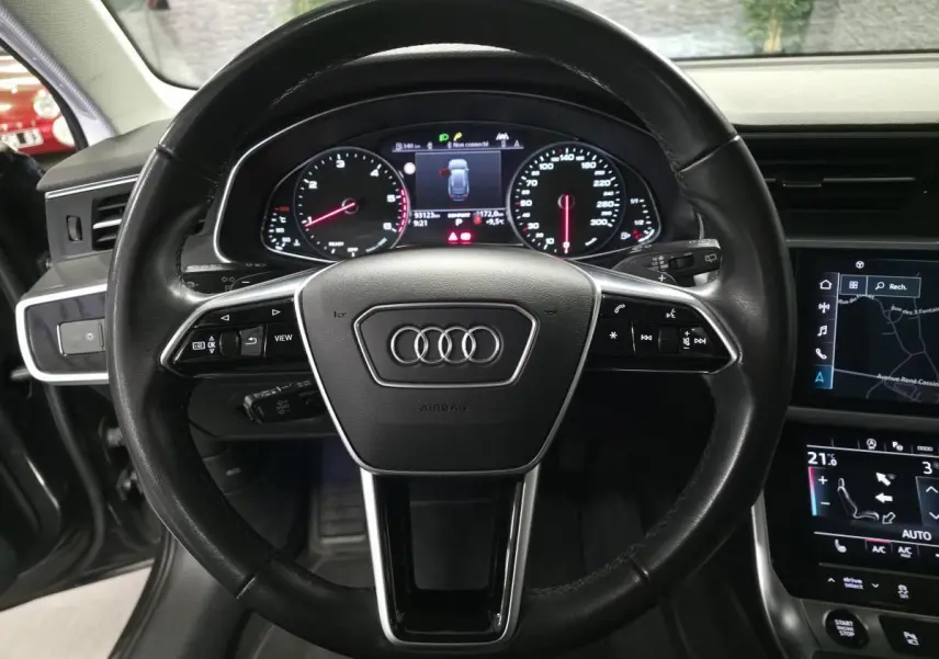 Vue intérieure centrée sur le volant noir en cuir d'une Audi A6 2022 avec tableau de bord digital et écran tactile.