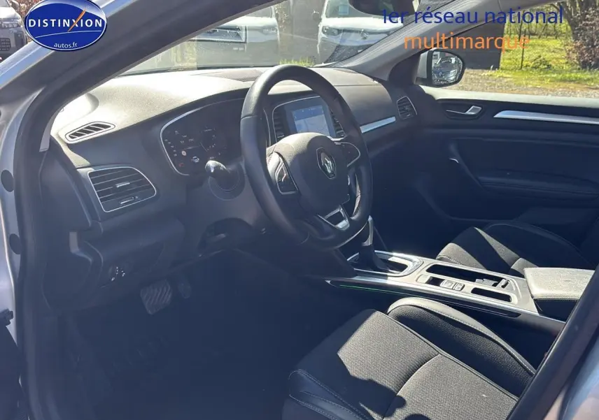 Intérieur côté conducteur de Renault Mégane IV 2023, volant multifonction et sièges tissu noirs visibles.