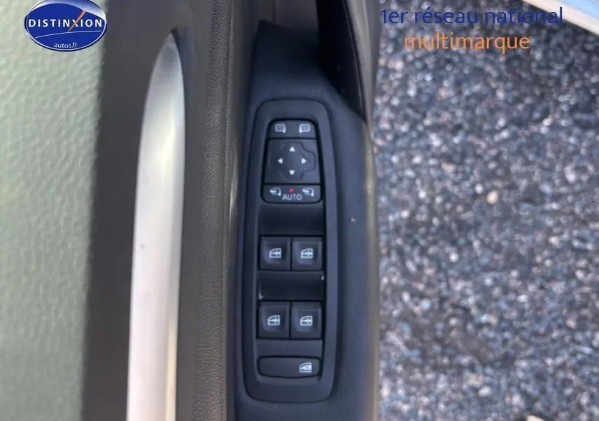 Gros plan sur la commande des vitres électriques côté conducteur d'une Renault Mégane IV gris Highland, avec fond bitume.