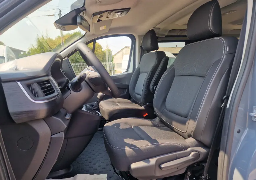 Vue intérieure côté conducteur du Renault Trafic Combi gris urbain 2026, montrant les sièges avant et le tableau de bord.