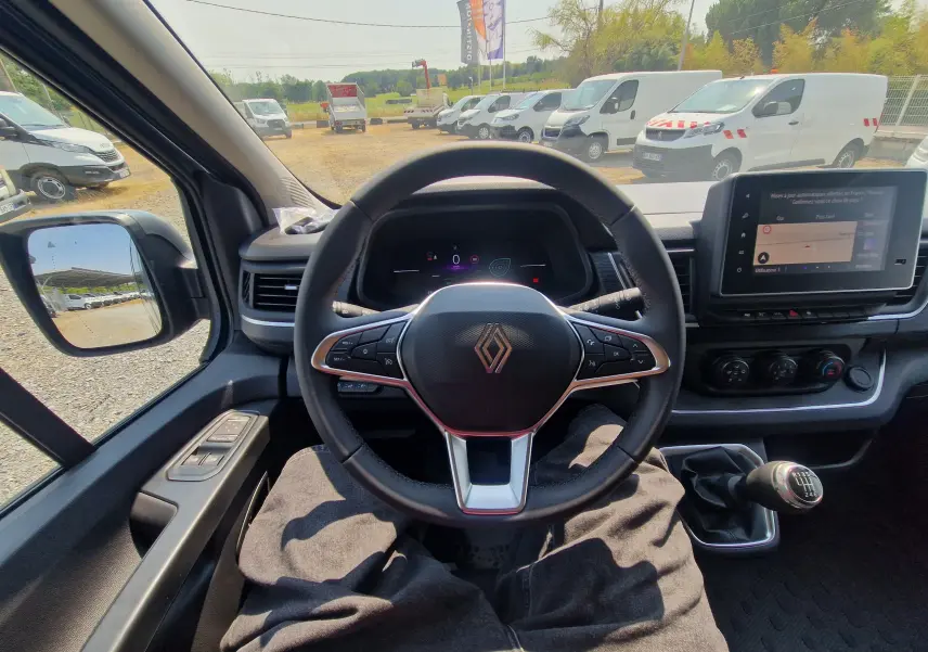 Vue intérieure centrée sur le volant Renault du Trafic Combi 2026, avec tableau de bord numérique et levier de vitesses manuel.