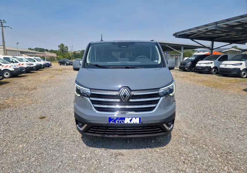 Vue frontale d’un Renault Trafic Combi gris urbain 2026, avec calandre chromée et plaque Zero KM visible.