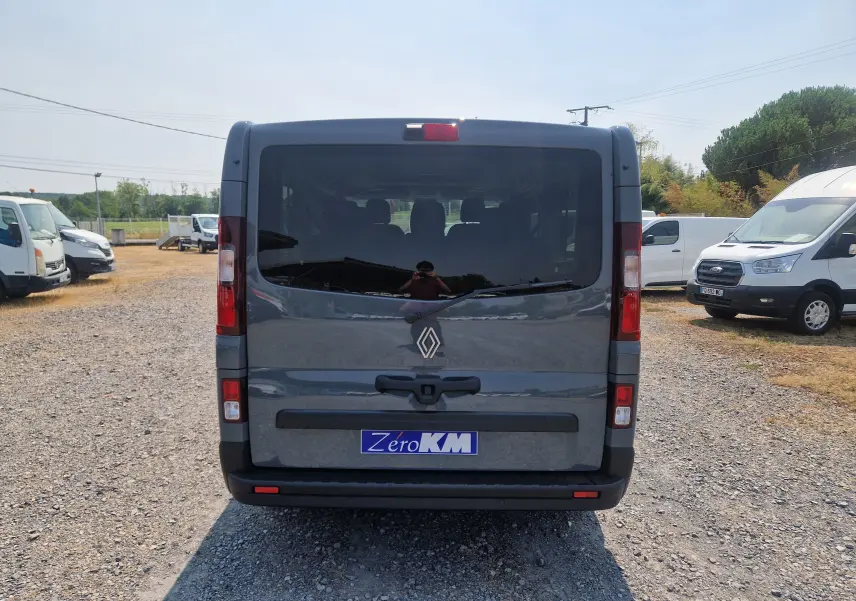 Vue arrière d'un Renault Trafic Combi gris urbain avec vitres teintées et plaque Zero KM visible.