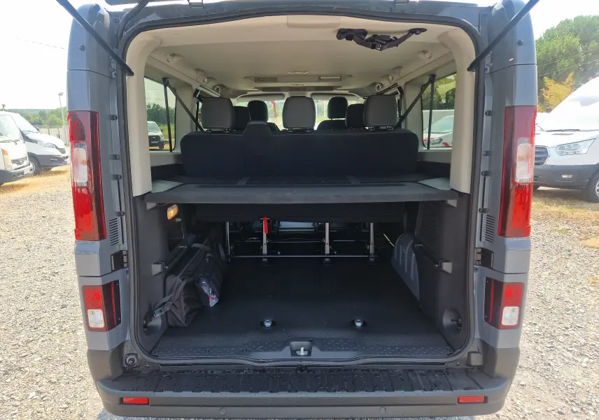 Vue arrière ouverte du Renault Trafic Combi gris urbain 2026, montrant l'espace de chargement avec sièges arrière et fixation fauteuil roulant.