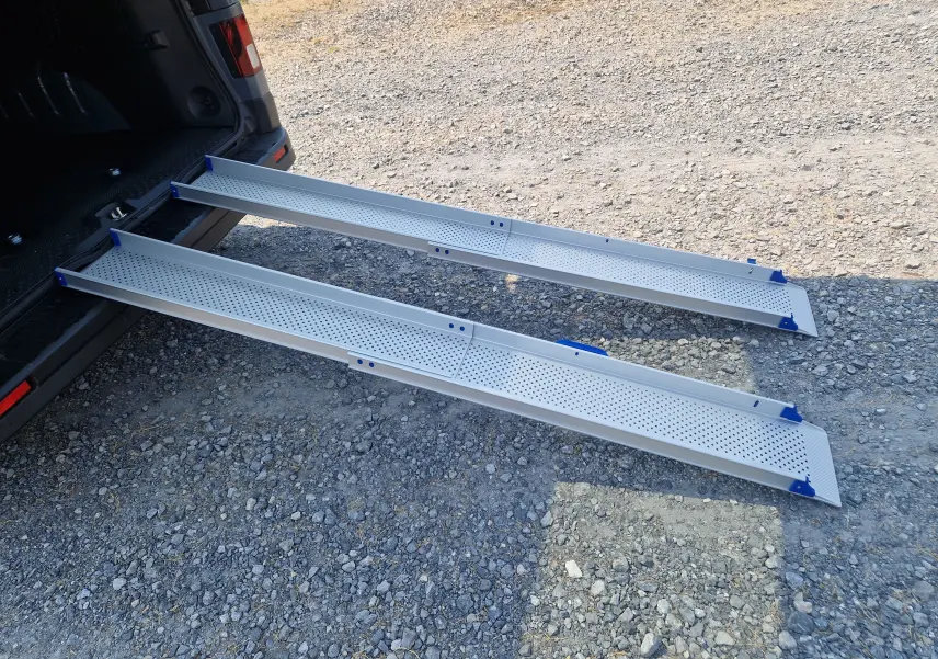 Vue arrière en 3/4 du Renault Trafic Combi gris urbain avec ses rampes d'accès amovibles en aluminium déployées au sol.