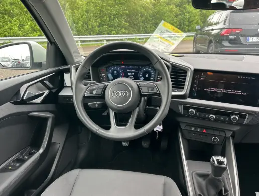 Vue intérieure centrée sur le volant cuir et le cockpit numérique de l'Audi A1 Sportback gris, avec boîte manuelle visible.