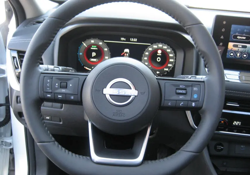 Vue rapprochée du volant noir du Nissan X-TRAIL blanc nacré 2026 avec tableau de bord numérique et écran central tactile.