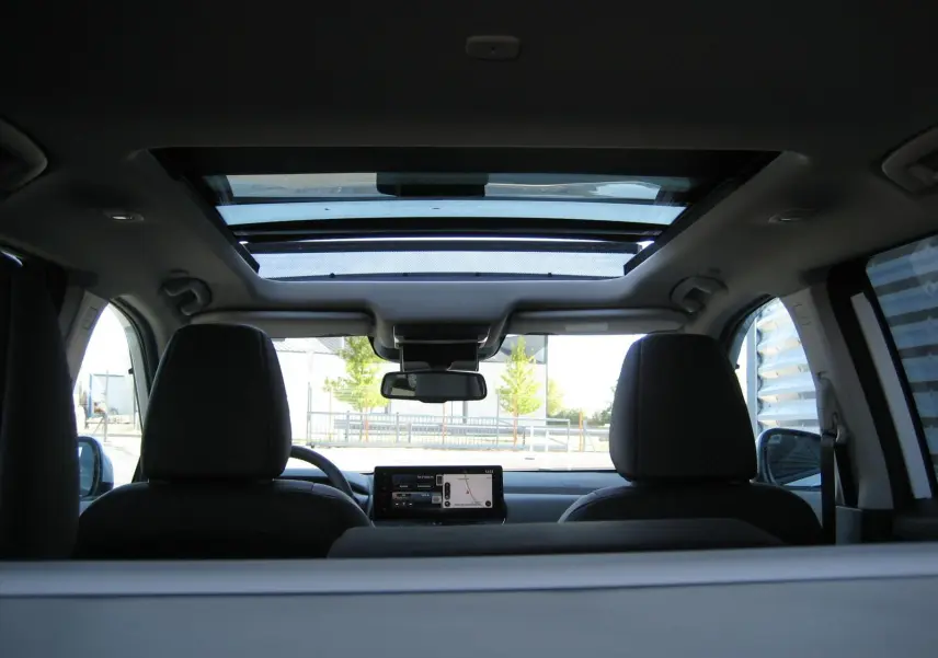 Vue intérieure arrière du Nissan X-Trail blanc nacré 2026, mettant en valeur le toit ouvrant panoramique et l'écran central.