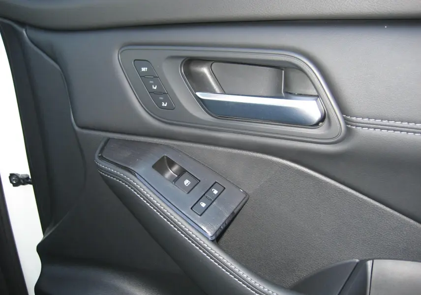 Gros plan sur la porte intérieure côté conducteur du Nissan X-TRAIL blanc nacré, avec commandes de fenêtre et poignée argentée.