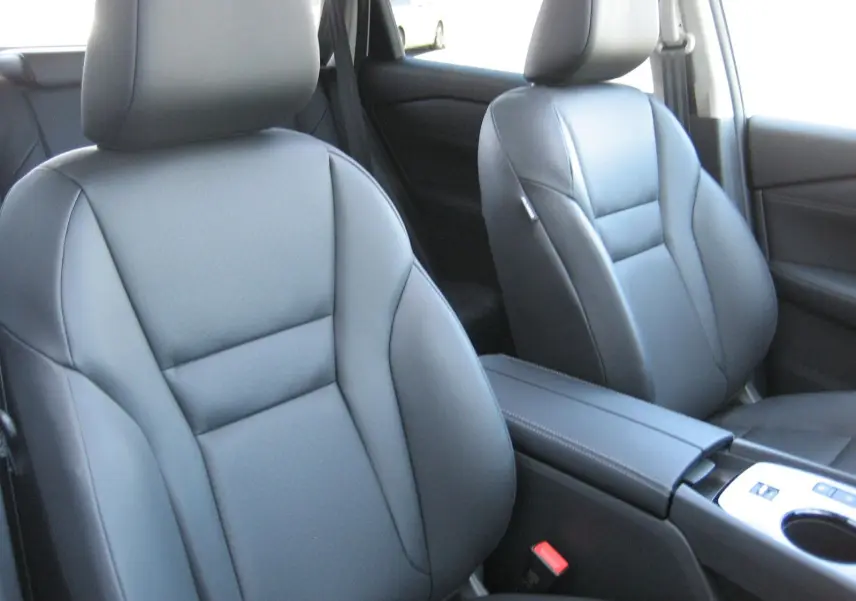 Vue intérieure rapprochée des sièges avant en cuir noir du Nissan X-Trail blanc nacré, avec console centrale visible.