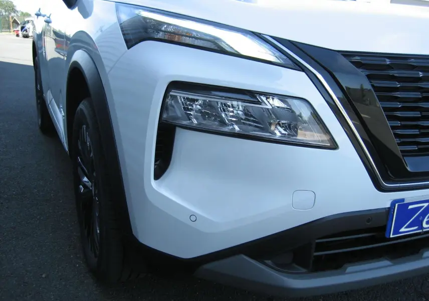 Gros plan sur l'avant droit du Nissan X-Trail blanc nacré, mettant en valeur le phare LED et la calandre noire.