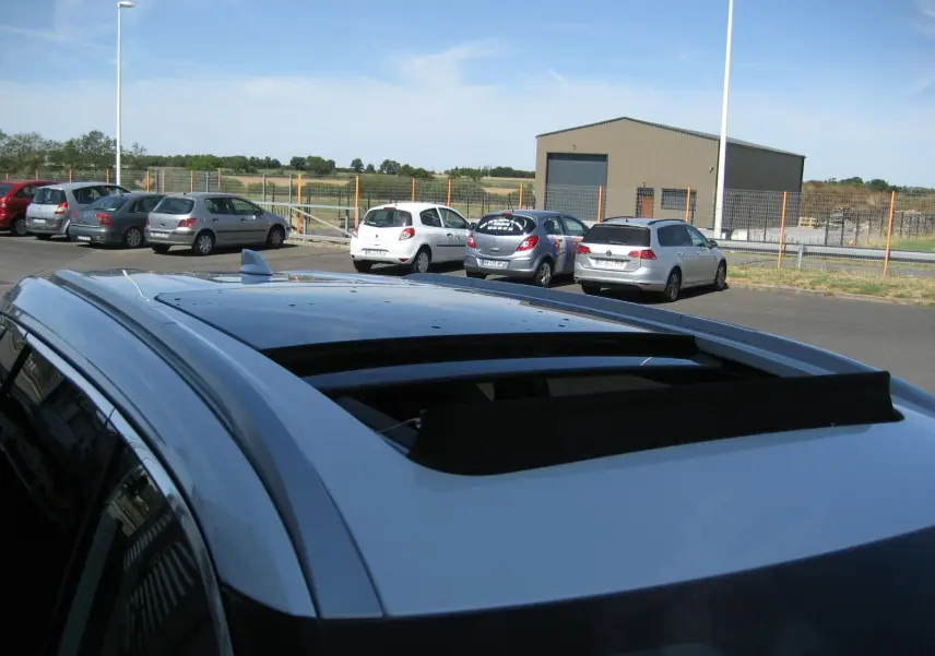 Toit ouvrant ouvert vu de dessus sur un Nissan X-TRAIL blanc nacré, avec barres de toit et antenne requin.