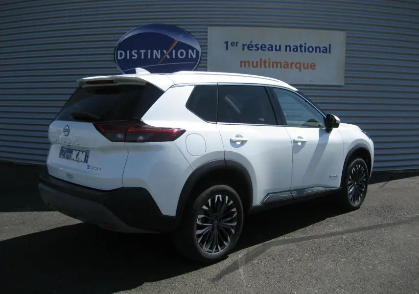 Nissan X-Trail blanc nacré vu en 3/4 arrière droit, avec jantes noires et toit blanc contrasté.