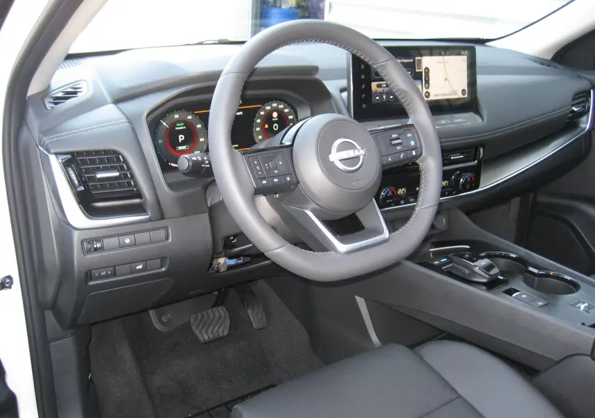 Vue intérieure côté conducteur du Nissan X-TRAIL blanc nacré 2026, avec volant multifonction et écran tactile central.