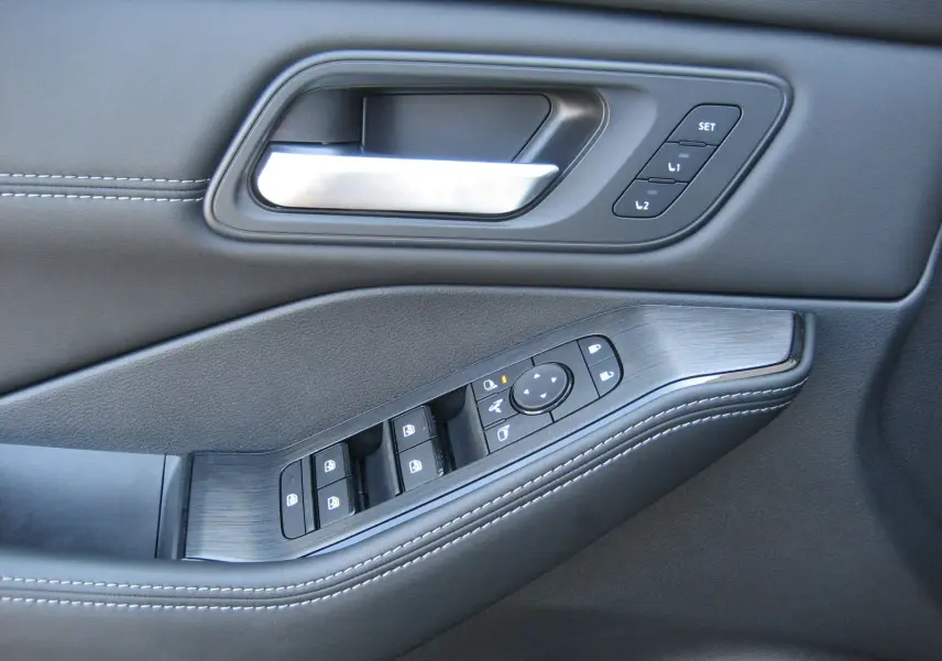 Gros plan sur la poignée intérieure et les commandes de porte en cuir noir avec surpiqûres blanches du Nissan X-Trail blanc nacré.