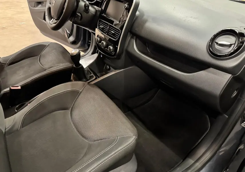 Intérieur avant droit d'une Renault Clio IV 2019, sièges tissu noir et tableau de bord gris foncé avec boîte manuelle.