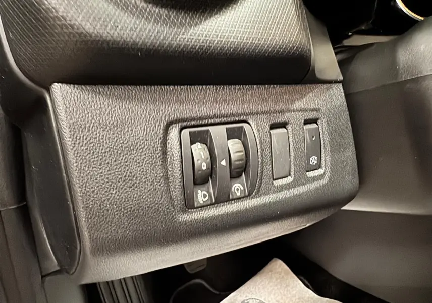 Gros plan sur les commandes d’éclairage et d’assistance au conducteur côté gauche du tableau de bord noir d’une Renault Clio IV gris foncé.