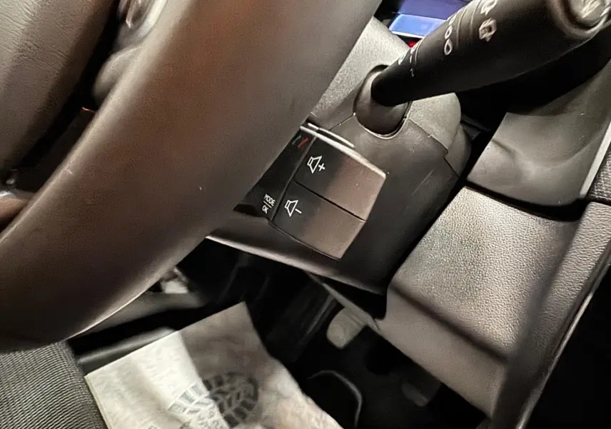 Vue rapprochée du volant et des commandes audio sur la colonne de direction d’une Renault Clio IV gris foncé.