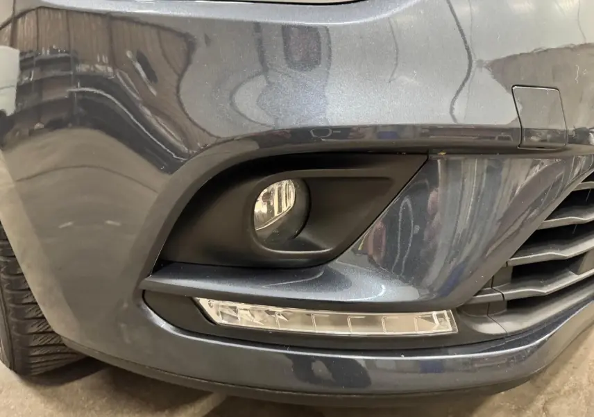 Gros plan sur le pare-chocs avant droit gris foncé métallisé de la Renault Clio IV avec antibrouillard et feux LED intégrés.