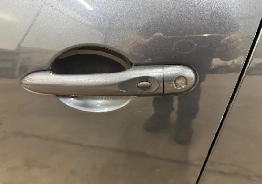Poignée de porte côté gauche d'une Renault Clio IV gris foncé métallisé avec bouton de verrouillage intégré.
