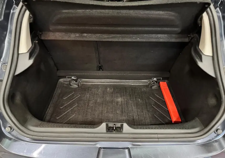 Coffre ouvert d’une Renault Clio IV gris foncé, montrant un tapis de coffre noir avec un triangle de sécurité rouge.