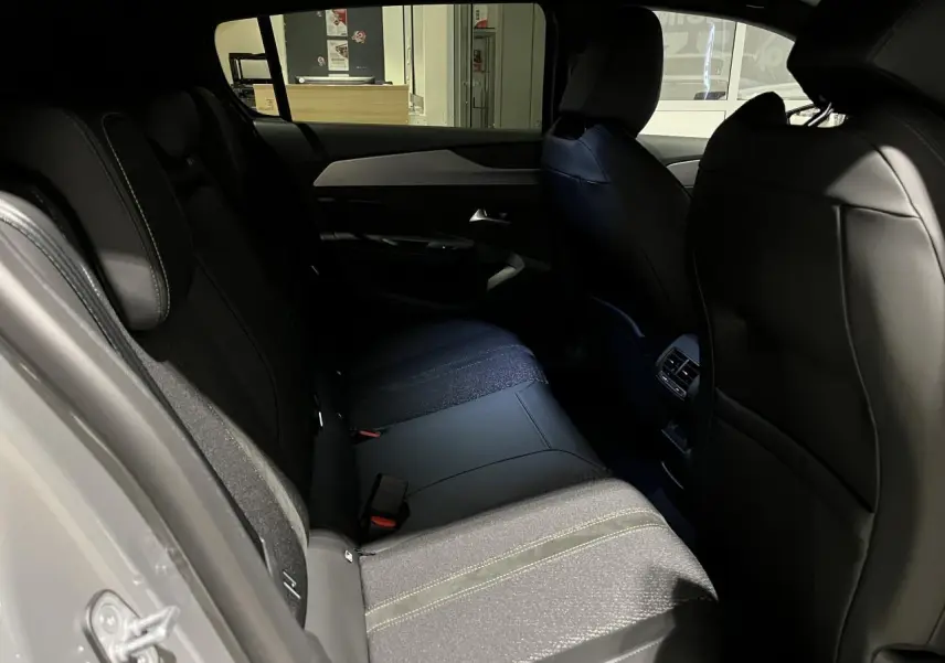Vue intérieure arrière droite de la Peugeot 308 GT 2024 avec sellerie tri matières noire et surpiqûres vertes.
