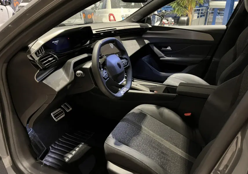 Intérieur avant droit de la Peugeot 308 GT 2024 gris selenium, volant cuir et planche de bord moderne avec écran numérique.