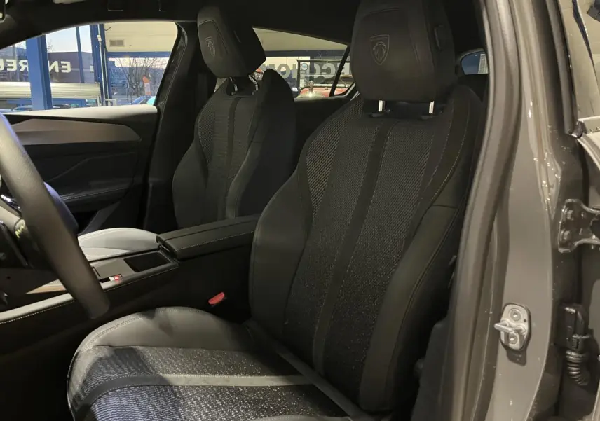 Vue intérieure côté conducteur de la Peugeot 308 GT 2024 gris selenium, sièges sport tri matières avec logo Lion brodé.