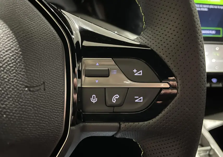 Gros plan sur les commandes gauche du volant cuir perforé de la Peugeot 308 GT 2024 gris selenium.