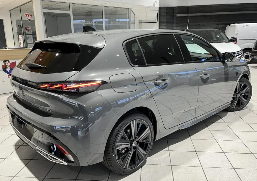 Peugeot 308 GT gris sélénium vue 3/4 arrière droit en intérieur avec jantes alliage noires et feux LED griffés.