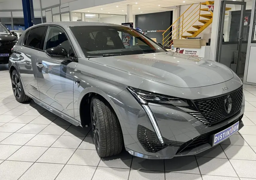 Peugeot 308 Gris Selenium vue 3/4 avant droit, calandre noire vernie et feux LED griffés en showroom.