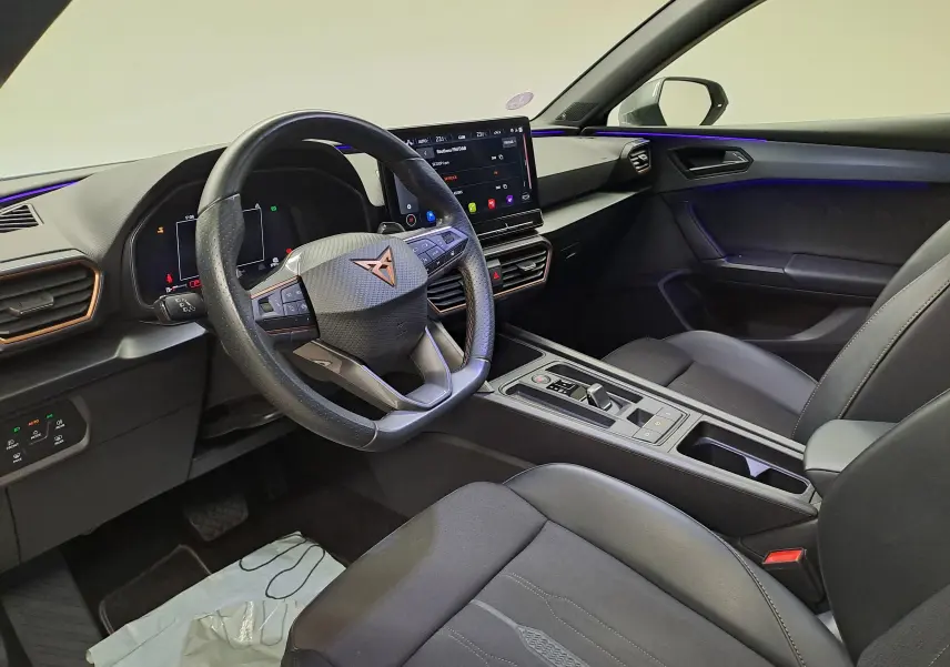 Intérieur avant droit de la CUPRA Leon 2023 noir, avec tableau de bord numérique et éclairage d'ambiance violet.