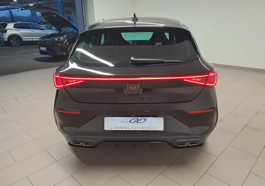 Vue arrière d'une CUPRA Leon 1.5 TSI 150 DS7 V 2023 en noir minuit avec feux arrière LED allumés et double sortie d'échappement.