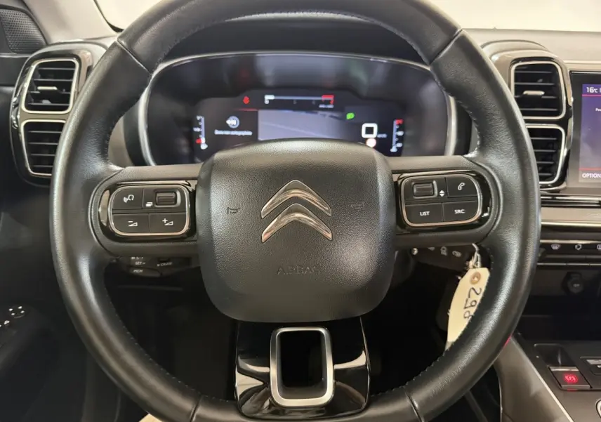 Vue rapprochée du volant cuir noir multifonctions d’un Citroën C5 Aircross 2021 avec tableau de bord numérique en arrière-plan.