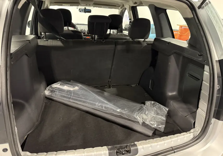 Vue depuis le coffre ouvert du Dacia Duster gris 2011, montrant l’espace de chargement avec un objet emballé en plastique.