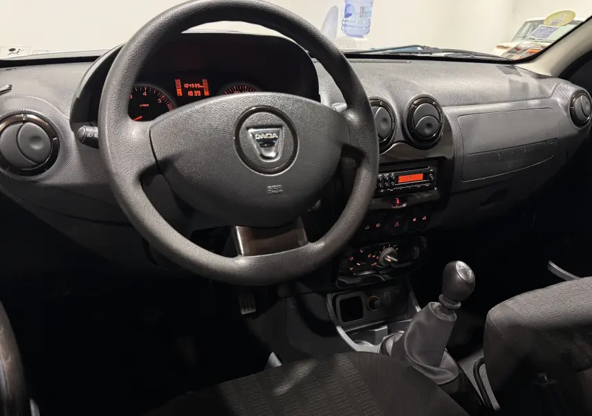 Vue intérieure du tableau de bord et volant noir du Dacia Duster gris, avec levier de vitesses manuel visible.