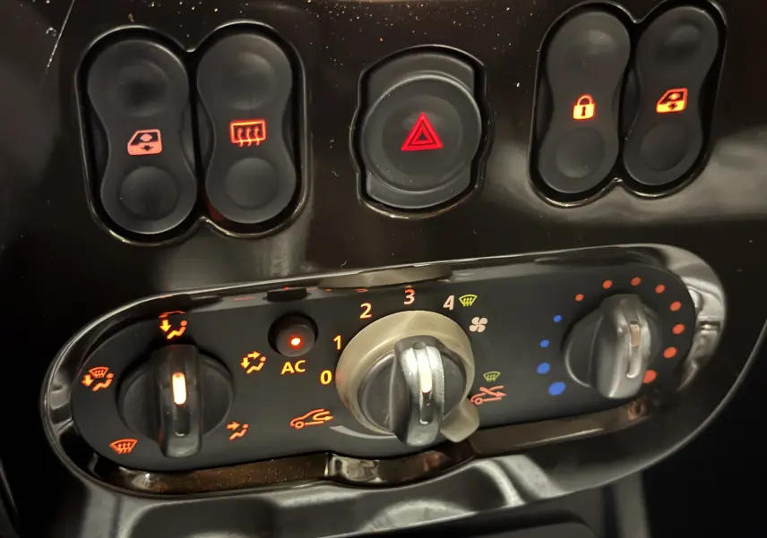 Gros plan sur la console centrale du Dacia Duster gris 2011, montrant les commandes de climatisation et les boutons de verrouillage.