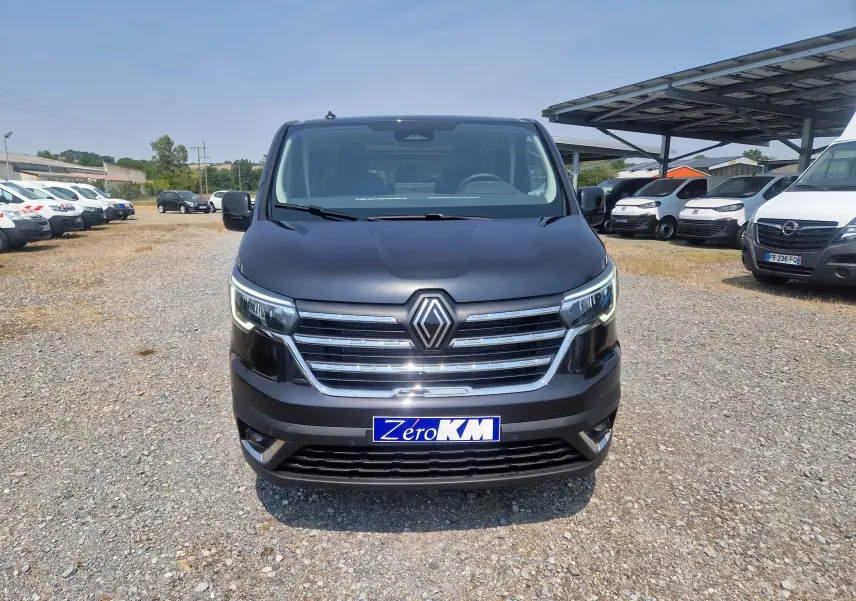 Vue avant d'un Renault Trafic Combi noir 2026 avec calandre chromée et plaque "Zéro KM" sur un parking extérieur.