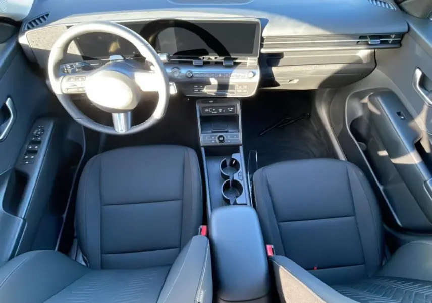 Vue intérieure avant du Hyundai Kona 2025 hybride, sièges noirs, volant multifonction et grand écran numérique.