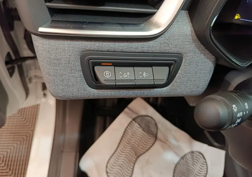 Détail intérieur côté gauche de la planche de bord grise avec commandes de réglage des phares et verrouillage sur Renault Clio blanche.
