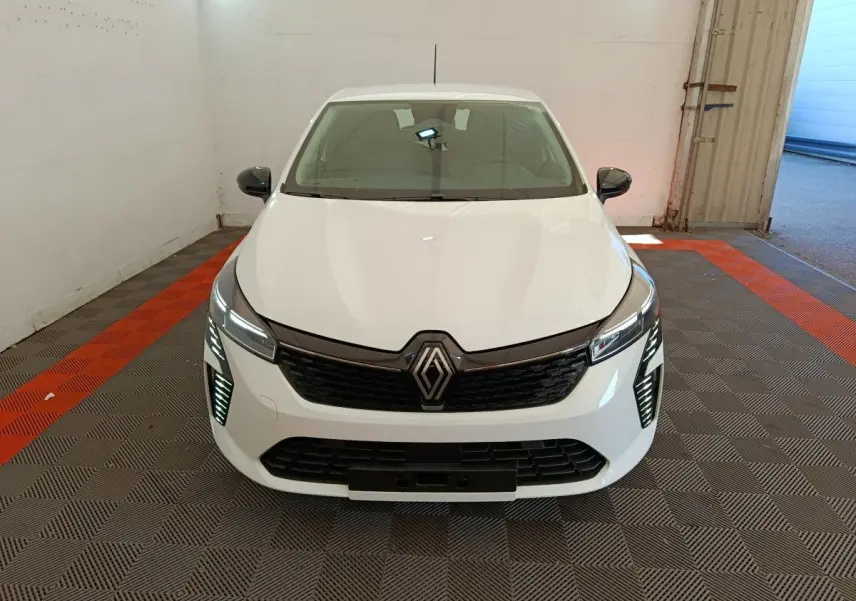 Vue avant d'une Renault Clio blanche 2024 avec feux LED allumés et calandre noire brillante dans un garage.