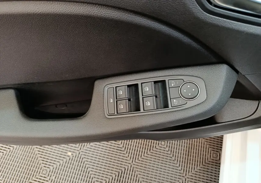 Vue rapprochée des commandes de lève-vitres et réglages des rétroviseurs sur la porte côté conducteur d'une Renault Clio blanche.