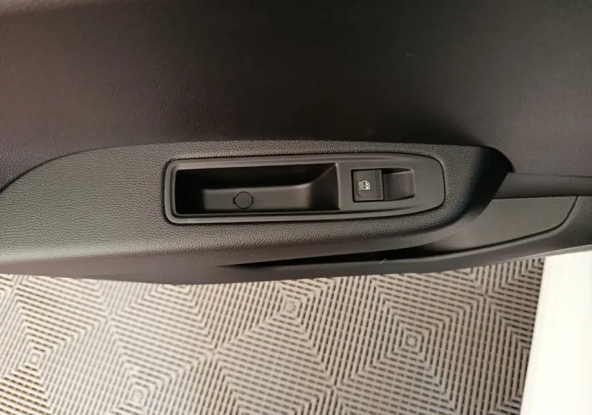 Détail de la commande de verrouillage de porte noire sur la portière intérieure d'une Renault Clio blanche.